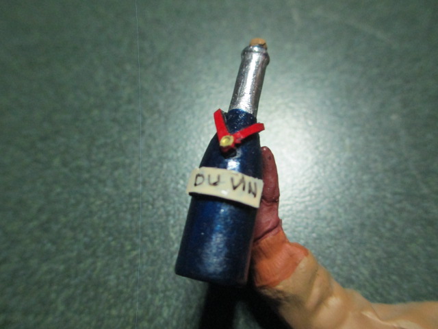 Paint stripped off of the bottle neck to show the 'foil'.  Ribbon and label cut from thin rubber and glued into place.  Crowned with a 'gold' button on the ribbon.